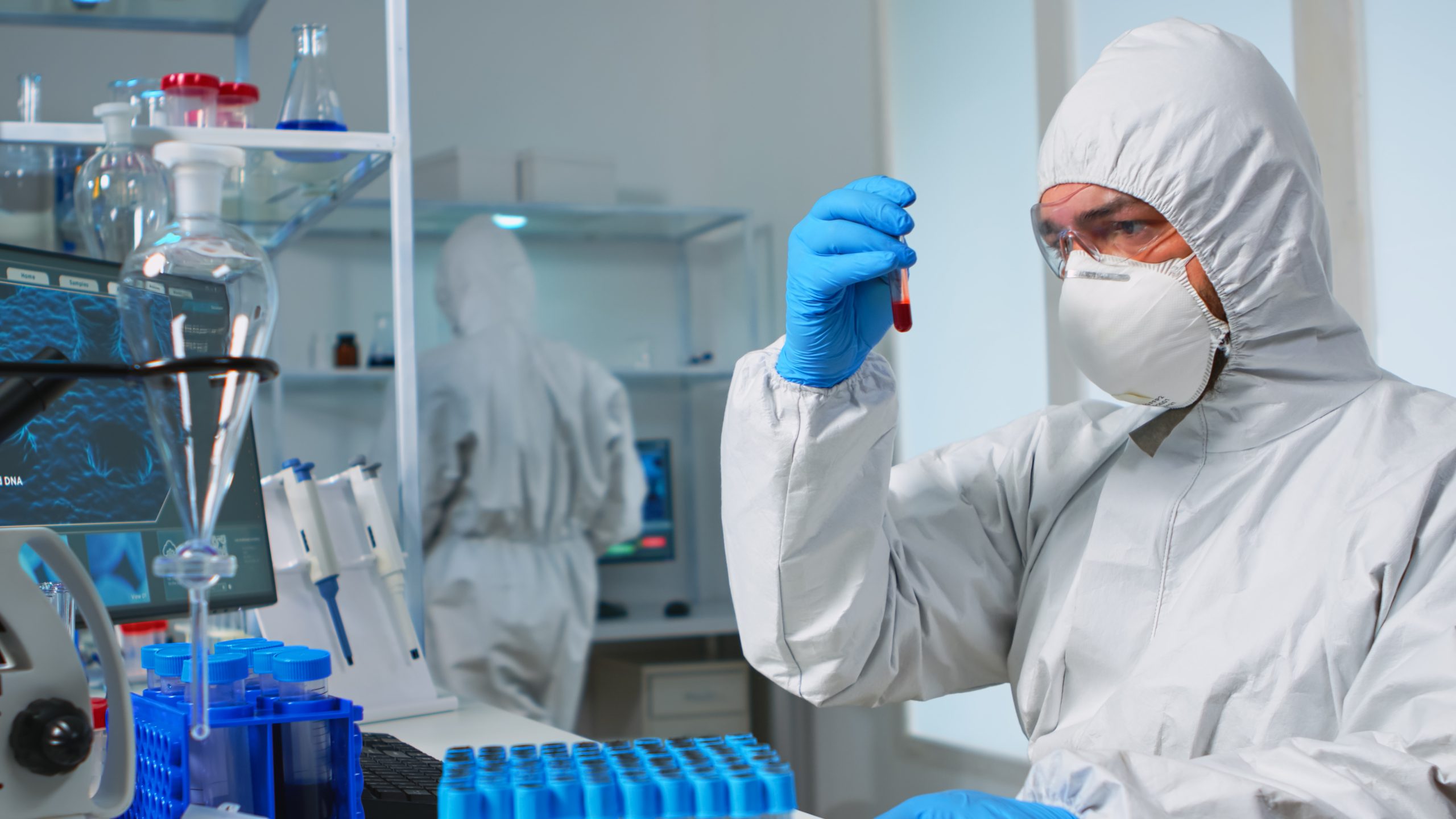 Investigador con traje de protección y mascarilla sosteniendo un tubo con una muestra de sangre