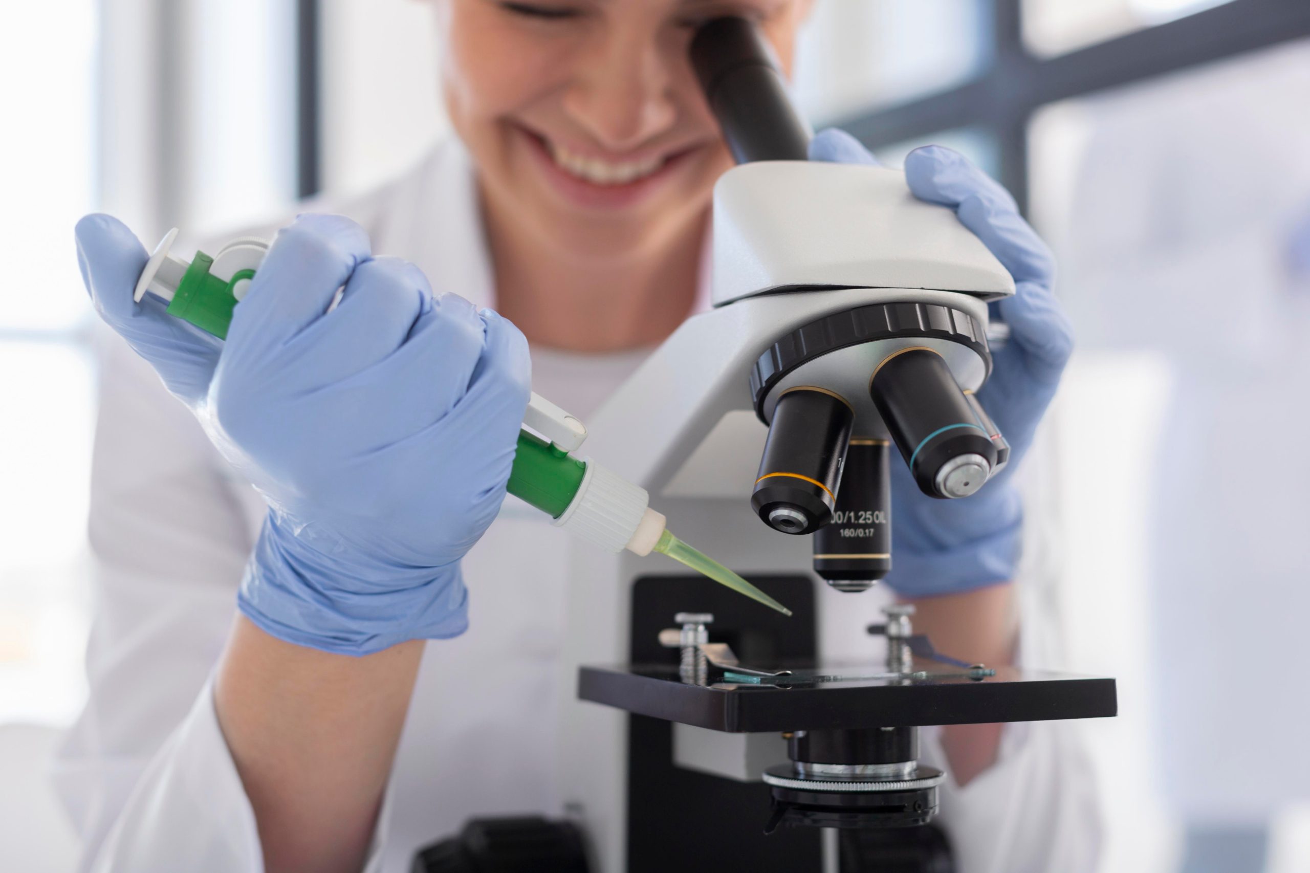 Mano con guante dejando caer una gota con una pipeta bajo un microscopio